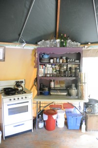 Knick knack cabinet with spice jars, handmade pottery, and cookbooks in a portable tent shelter called a Yome