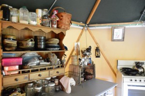 Knick knack cabinet with spice jars, handmade pottery, and cookbooks in a portable tent shelter called a Yome