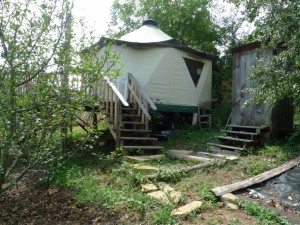 Outhouse, walking path, and Yome style yurt home with large deck at the edge of the forest
