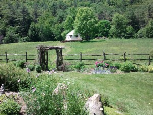 Landscape photo of Yome tent yurt home in the distance in a pasture with wildflowers and natural wood arch and fence