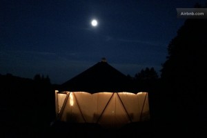 Glowing photo of nighttime Yome style yurt dwelling illuminated from within with large full moon in the distance