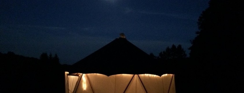 Glowing photo of nighttime Yome style yurt dwelling illuminated from within with large full moon in the distance