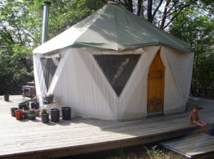 Yurt like tent home on broad deck with small child and plantings